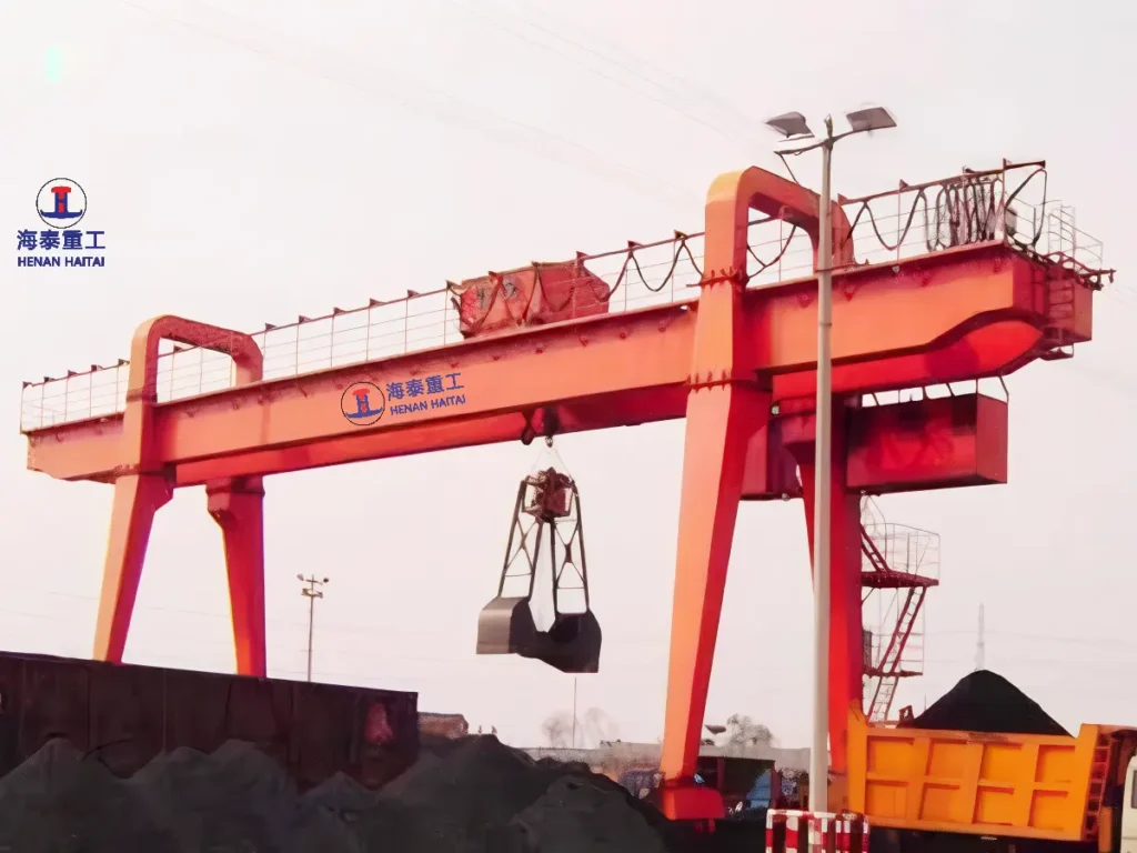 Double girder gantry crane fitted with a mechanical grab bucket, unloading bulk coal from a truck at an industrial yard