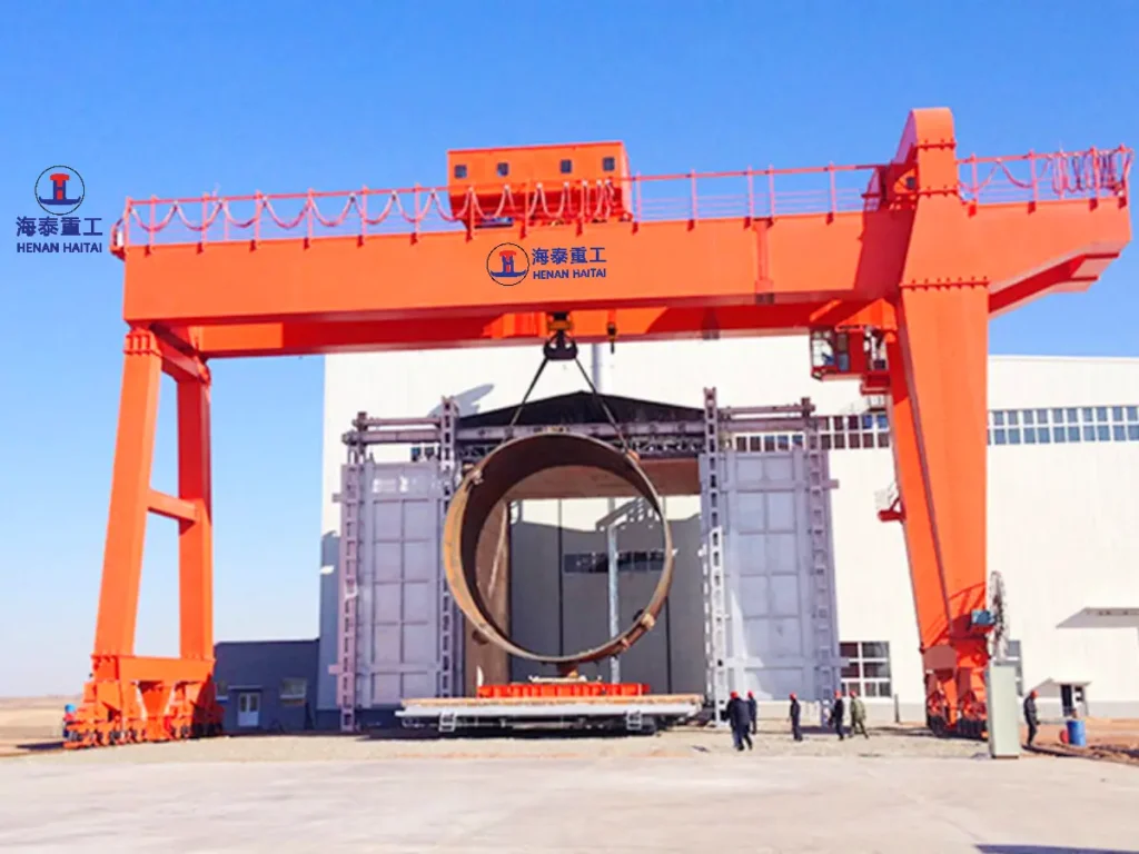 Double girder gantry crane lifting a large cylindrical steel component at an industrial fabrication site