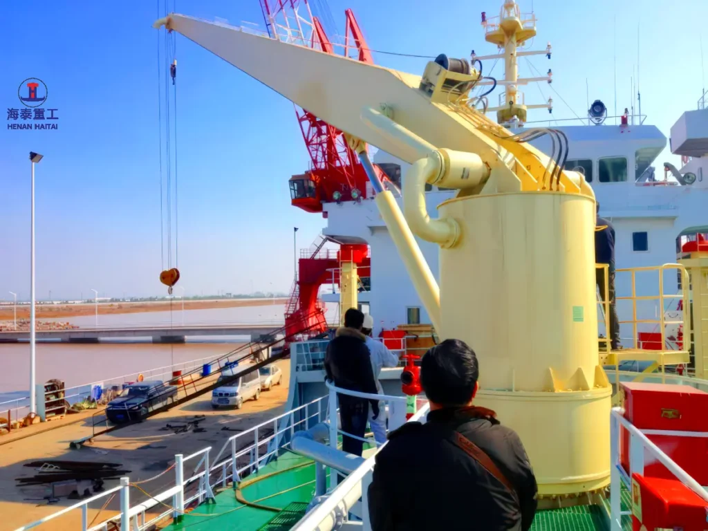 Close-up of a hydraulic stiff boom marine crane pedestal and boom mounted on a vessel deck at quayside, viewed from above